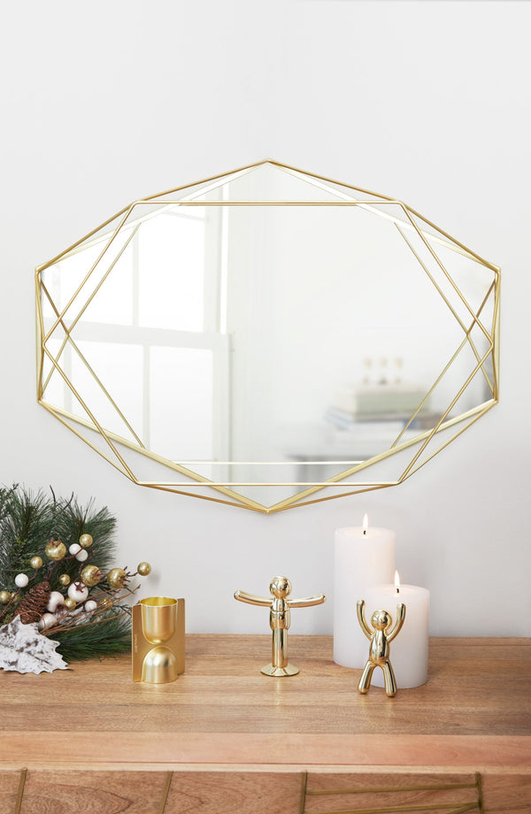 A contemporary geometric mirror from the Umbra range, known as the Prisma Mirror - Brass, placed on a table alongside candles and a Christmas tree.