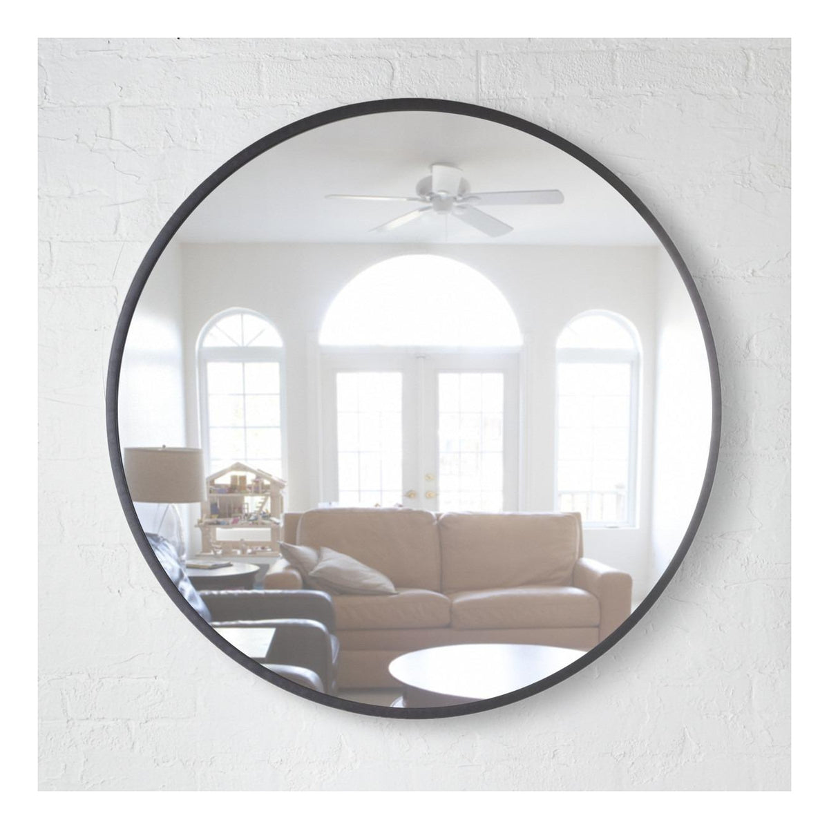 Umbra Hub 94cm round mirror in black on a white brick wall, reflecting a lounge
