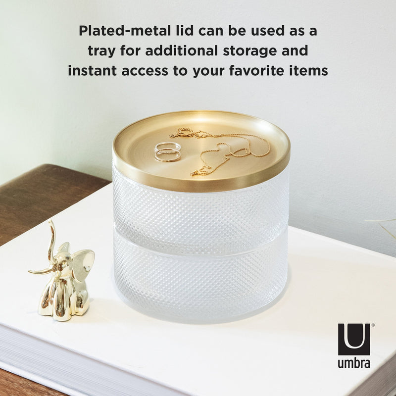 The Umbra TESORA STORAGE BOX is a modern design storage solution that includes a gold plated metal lid, providing instant access to your favorite items while also serving as a tray for additional storage.